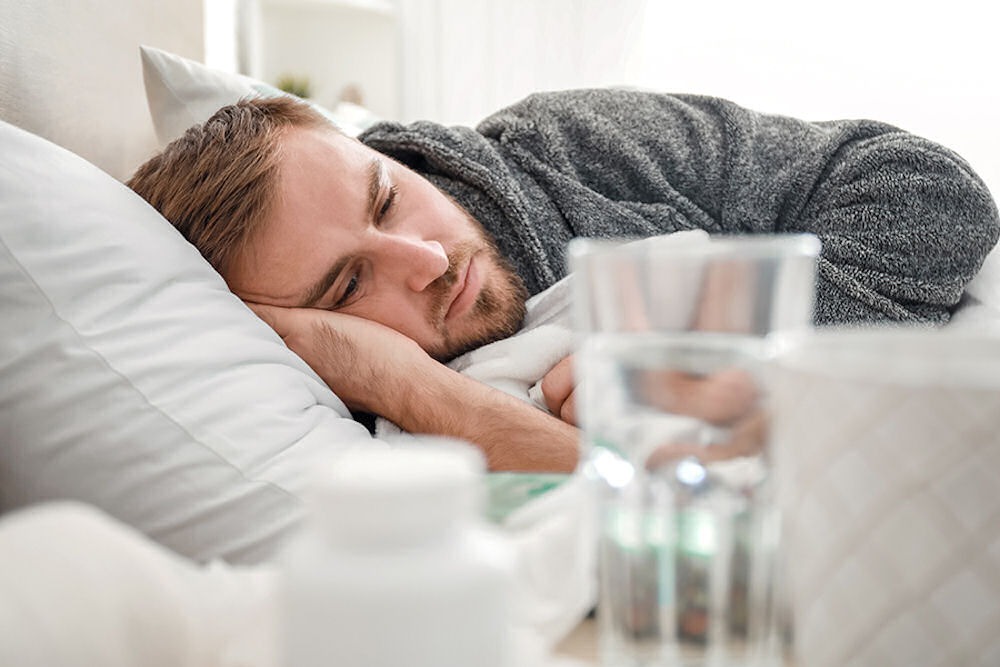 Man lying down from scromiting, with medications and water next to him on the bed.