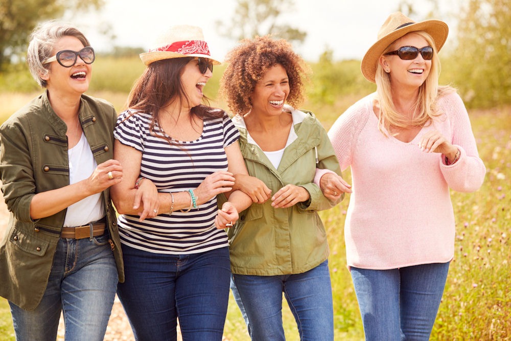 Group of four women walking on a trail with linked arms.