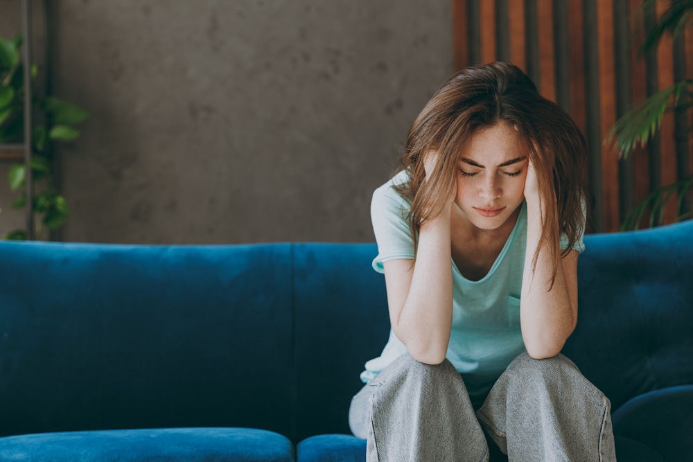Women on peacock blue couch holding head while receiving treatment for chronic stress.