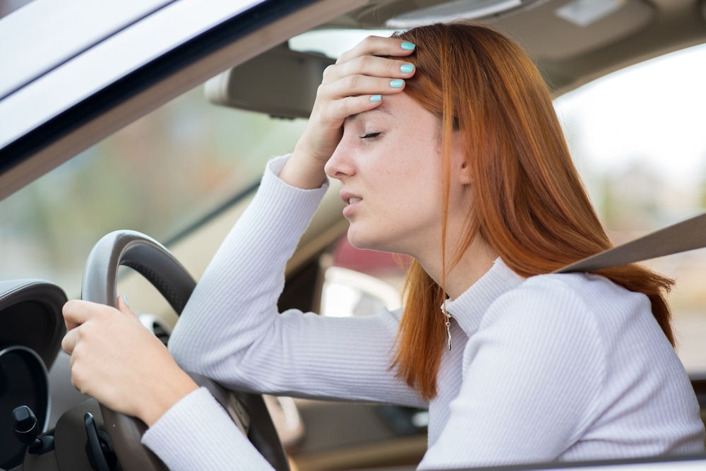 Woman with red hair and greenish-blue nails holding forehead in frustration while driving.